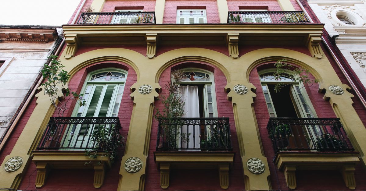 Fachada de un edificio reciclado con balcones de hierro en una calle arbolada